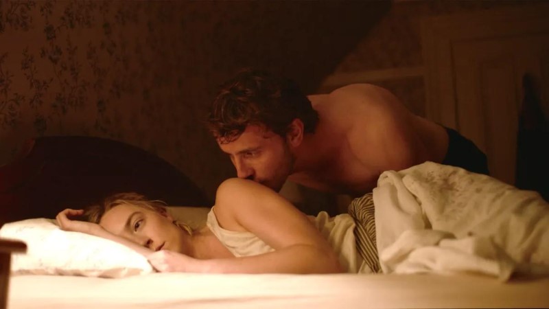 Homem beija braço da esposa deitada na cama.