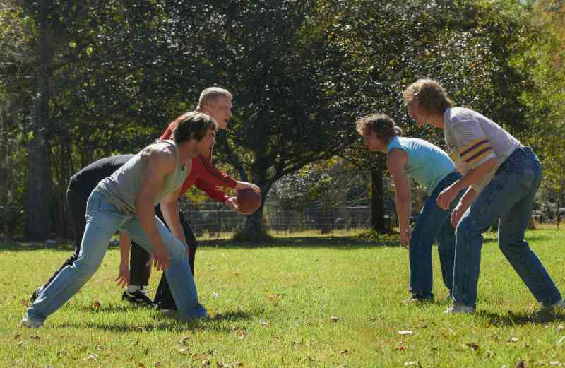 Cinco homens treinando rúgbi num parque.