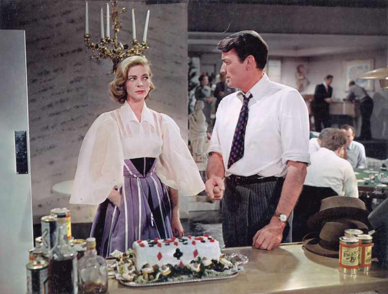 Lauren Bacall e Gregory Peck trocando olhares diante de um bolo.