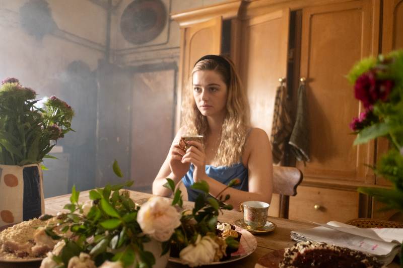 Garota adolescente sentada à mesa com uma xícara de chá na mão