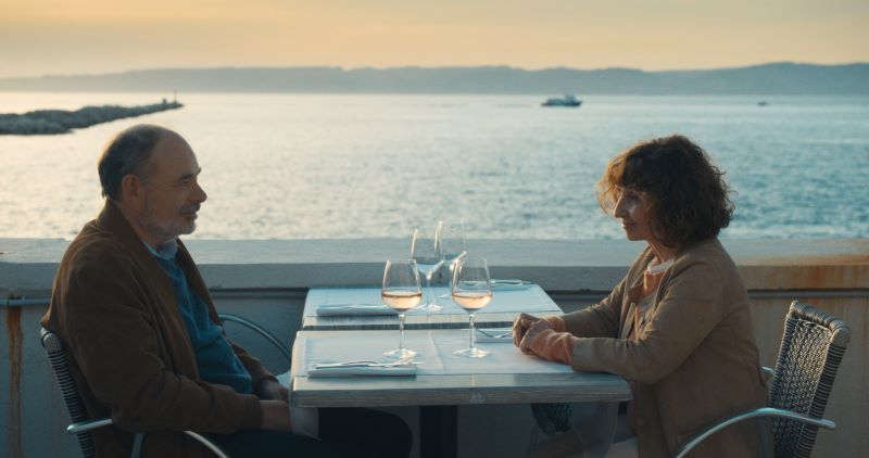 Um homem e uma mulher da terceira idade sentados à mesa em frente ao mar.