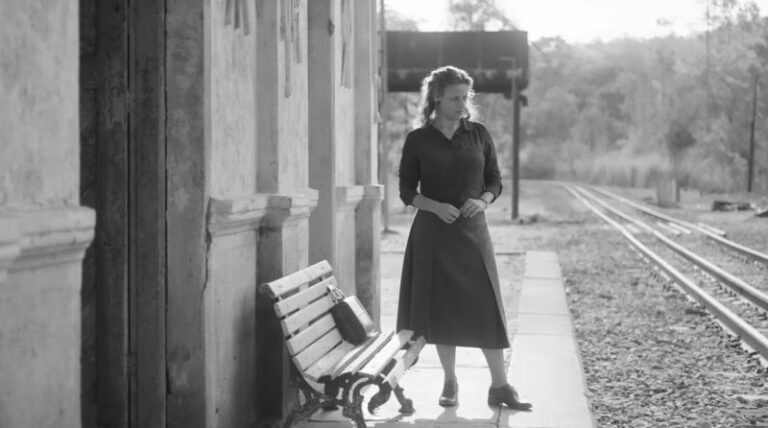 Mullher com vestido espera na estação de trem.