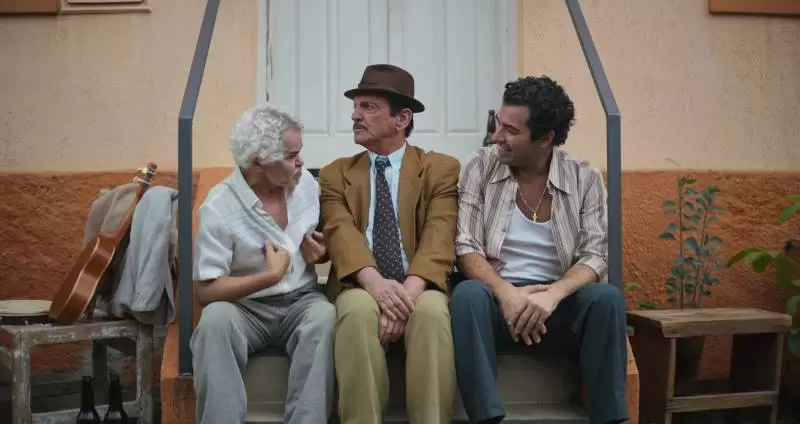 Gero Camilo, Paulo Miklos e Gustavo Machado sentados em uma escadaria.